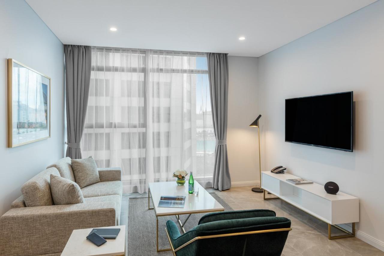 Meriton Suites Sussex Street, Sídney Exterior foto The photo shows a modern living room space with a light, airy ambiance. It features a comfortable beige sofa with decorative cushions, a sleek coffee table placed in front, and a dark green armchair. There is a large window covered with sheer curtain