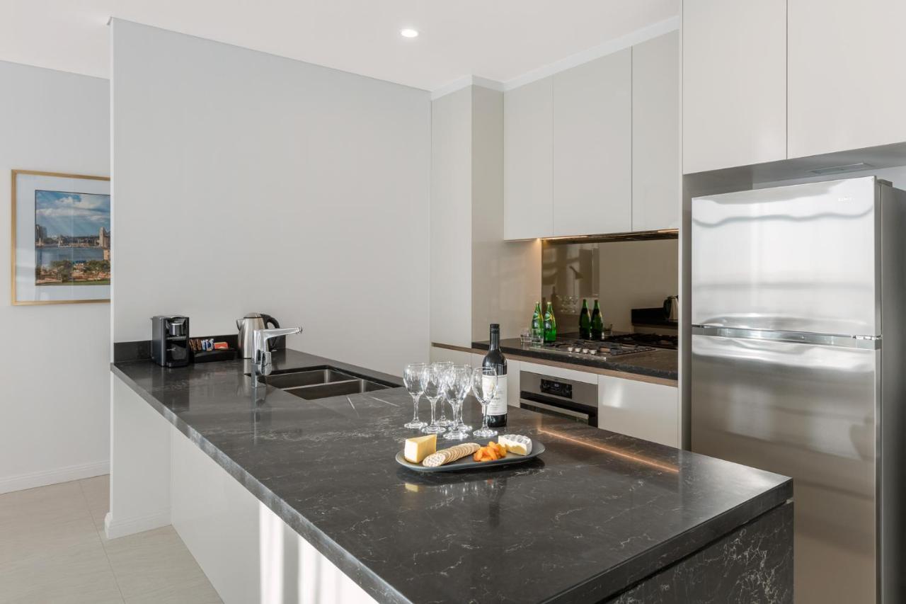 Meriton Suites Sussex Street, Sídney Exterior foto The photo shows a modern kitchen featuring a sleek design with a dark stone countertop. There is a built-in sink and possibly a cooktop. The kitchen cabinetry is light-colored, creating a contrast with the dark counter. On the countertop, there are w