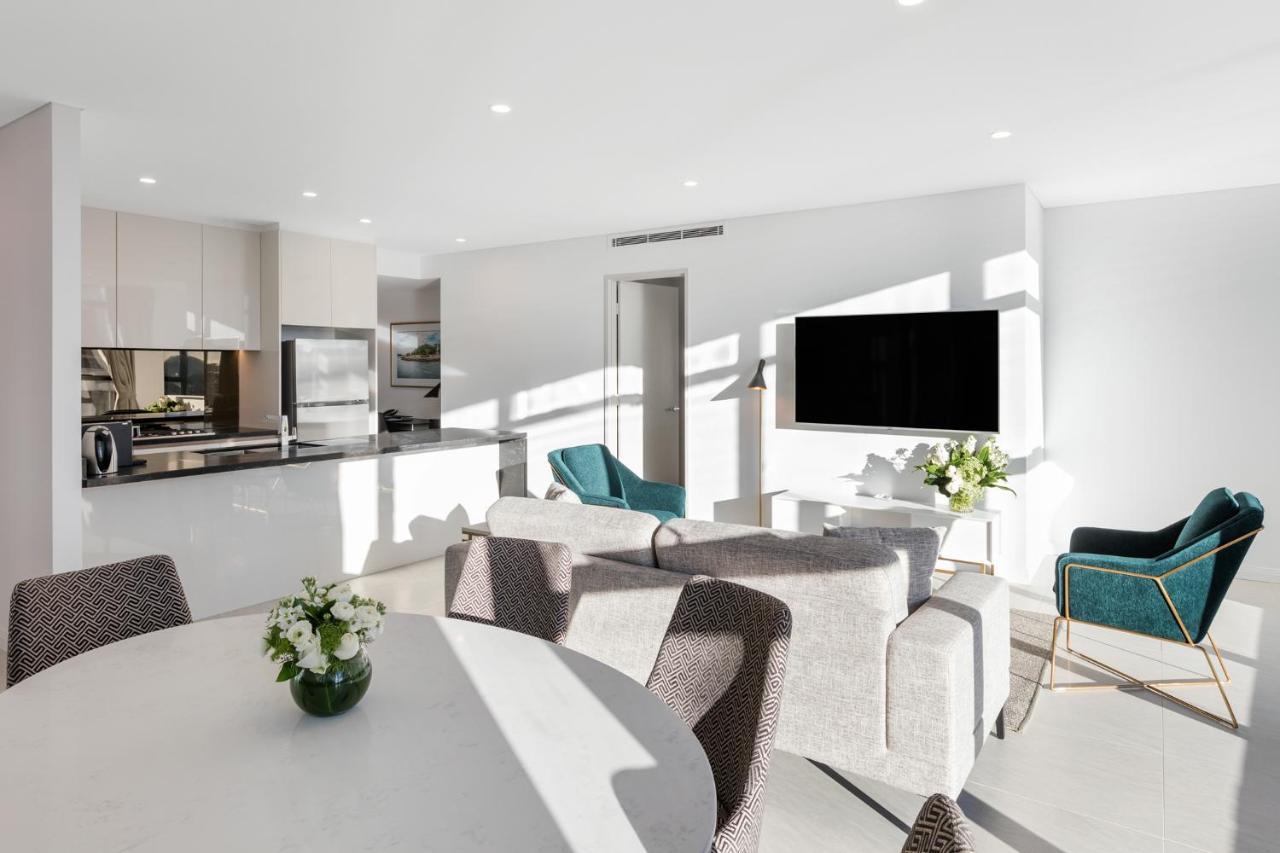 Meriton Suites Sussex Street, Sídney Exterior foto The photo shows a modern, bright living space that combines a kitchen and a living area. The kitchen features sleek cabinets and stainless steel appliances. In the foreground, there is a round dining table with a vase of flowers on it. Seating option