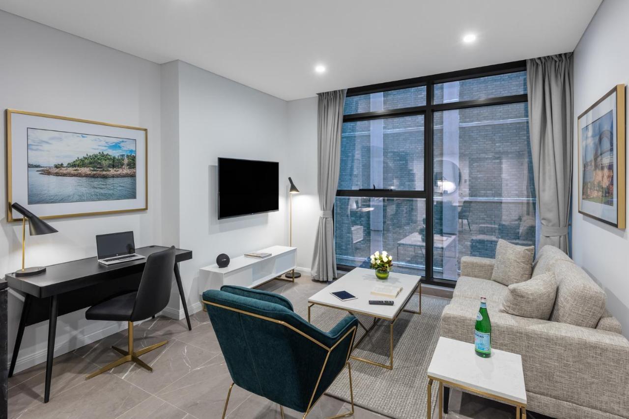 Meriton Suites Sussex Street, Sídney Exterior foto The photo shows a modern living area with a light color scheme. There is a comfortable seating arrangement that includes a beige sofa and an accent chair in teal. A coffee table is positioned in front of the sofa, with a small vase of flowers on it. 