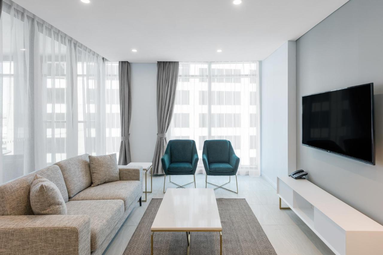 Meriton Suites Sussex Street, Sídney Exterior foto The photo shows a modern living room equipped with a light gray sofa, two teal chairs, and a coffee table in the center. The room features large windows with sheer curtains, allowing natural light to illuminate the space. There is a white media conso