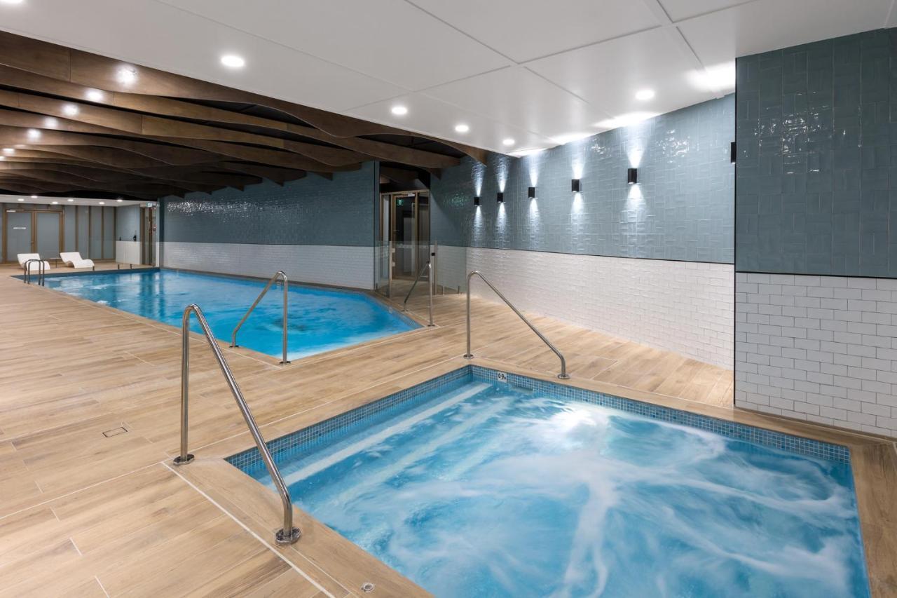 Meriton Suites Sussex Street, Sídney Exterior foto The photo shows a modern indoor spa area. There are two pools: one is larger and has a clear blue water, while the other is smaller, possibly a hot tub, with jets creating bubbles. The walls are a mix of blue tiles and white tiles, and the floor is m