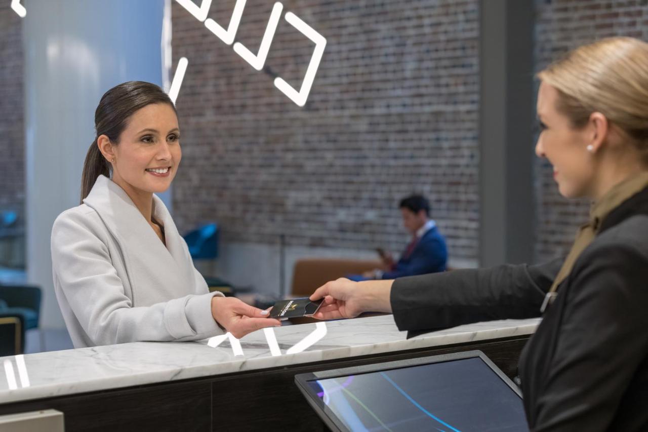 Meriton Suites Sussex Street, Sídney Exterior foto The image depicts a scene at a hotel reception desk. A woman with long hair, dressed in a white outfit, is smiling as she hands her card to a receptionist, who is in a black uniform. The reception area features a modern design, and there is a person 