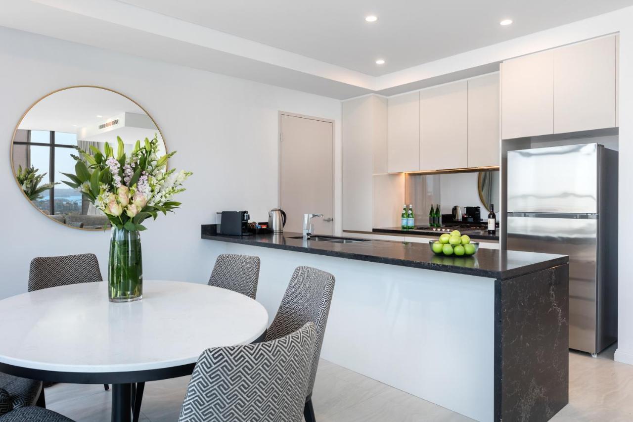 Meriton Suites Sussex Street, Sídney Exterior foto The photo shows a modern kitchen and dining area. In the foreground, there's a circular dining table surrounded by four stylish chairs. A large vase filled with fresh flowers is placed on the table, adding a touch of color and elegance. 

In the kitc