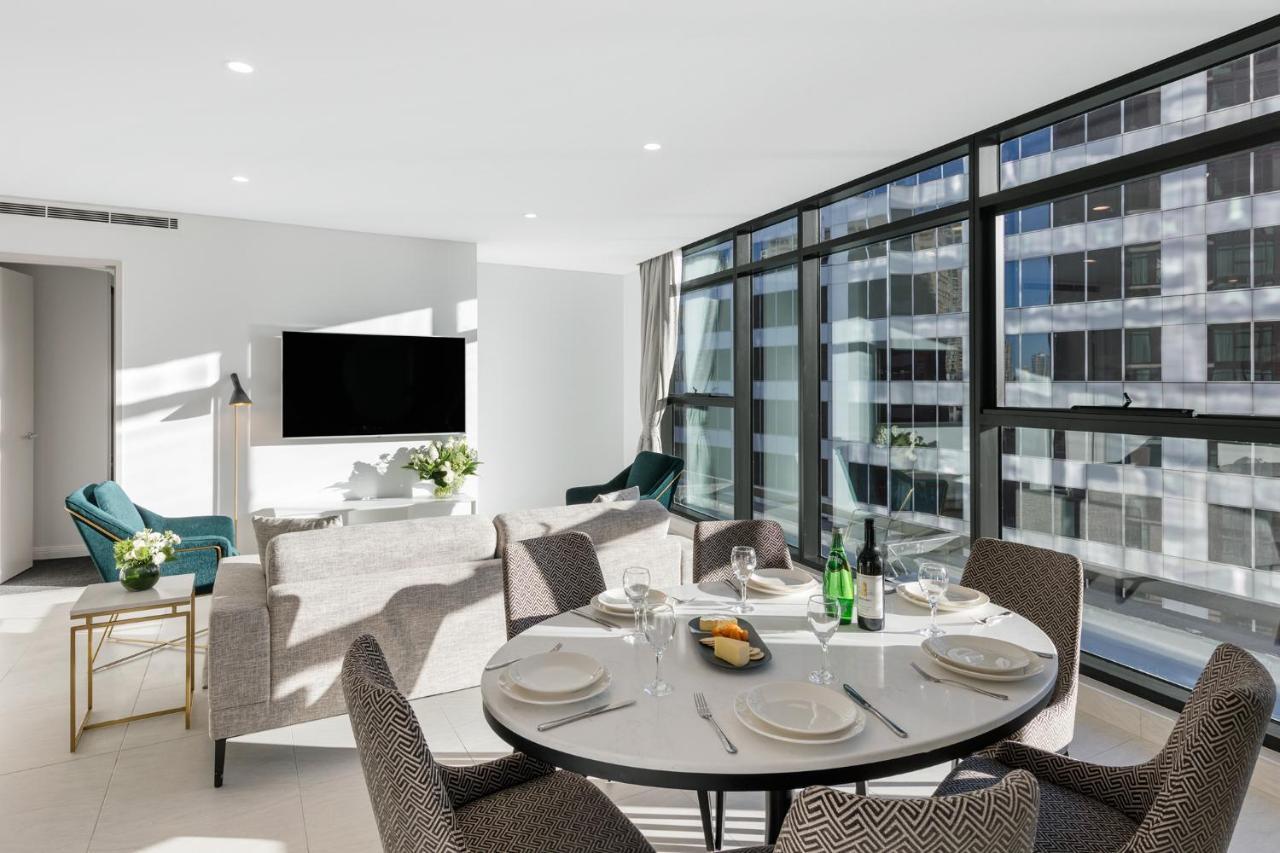 Meriton Suites Sussex Street, Sídney Exterior foto The photo shows a modern and stylish living room and dining area. In the foreground, there is a round dining table set for a meal with plates, cutlery, and drinks. The seating arrangement includes comfortable chairs around the table. 

In the backgro