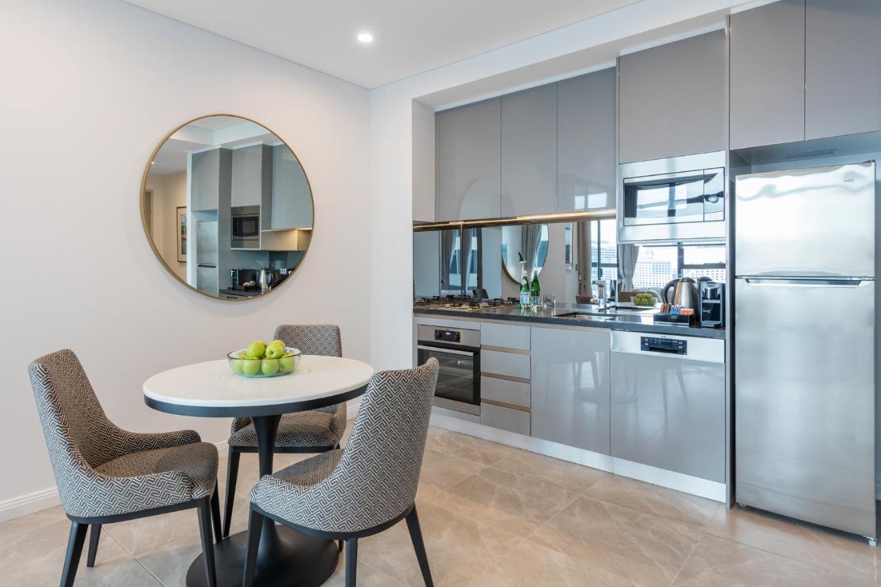 Meriton Suites Sussex Street, Sídney Exterior foto The photo features a modern kitchen and dining area. The kitchen has sleek grey cabinets and countertops, with built-in appliances including an oven and possibly a cooktop. There's a large stainless steel refrigerator on the right. A round dining tab