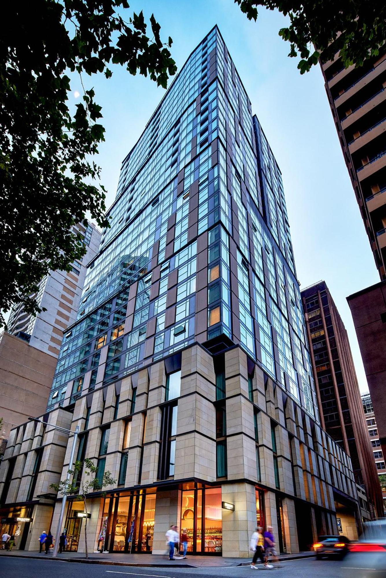 Meriton Suites Sussex Street, Sídney Exterior foto The photo shows a modern high-rise building with a sleek, glass facade reflecting its surroundings. The structure features a combination of glass and concrete materials, with multiple stories visible. The lower part of the building has a sturdy, text
