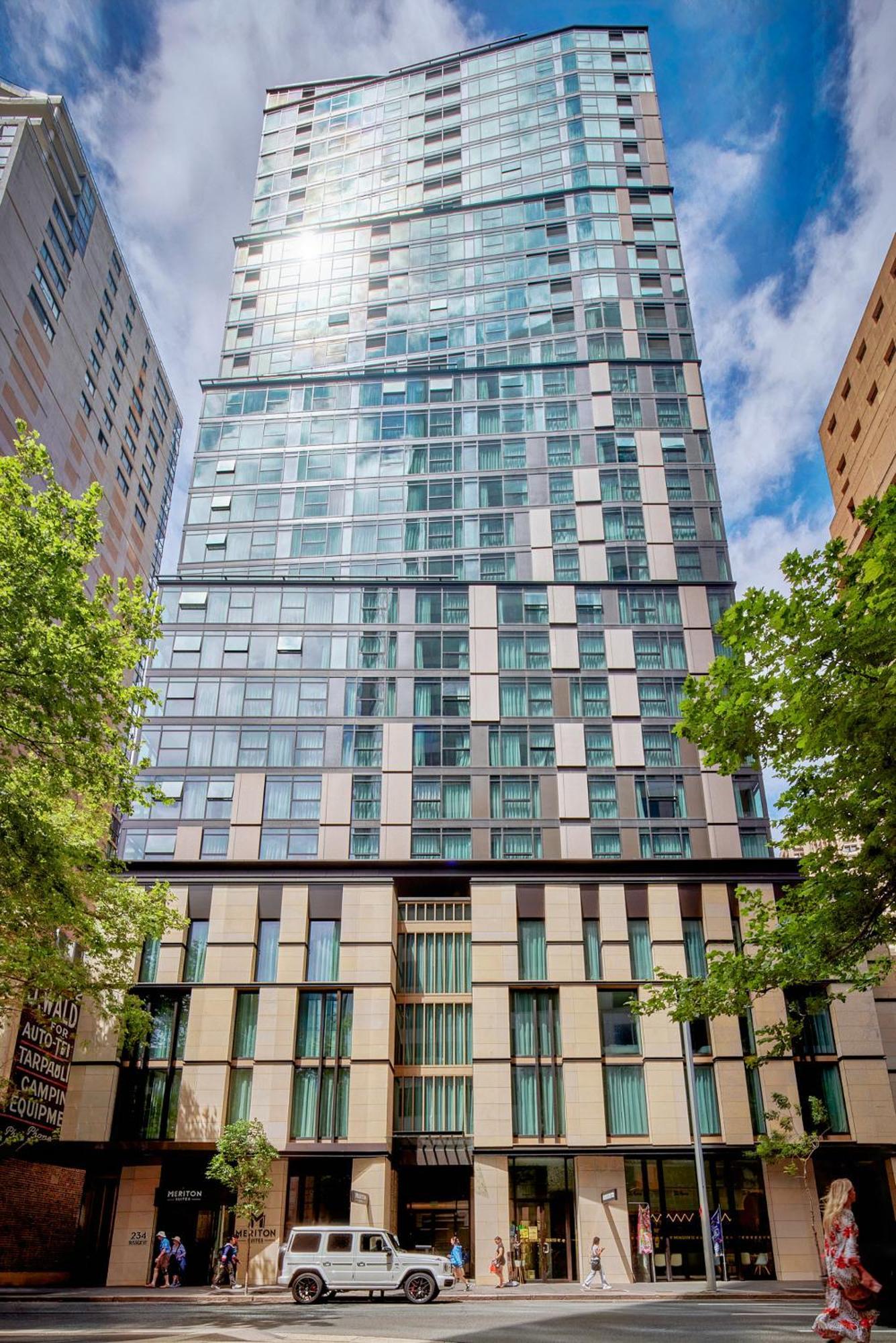 Meriton Suites Sussex Street, Sídney Exterior foto The photo shows a tall modern building with a glass facade and various architectural design elements. The structure has multiple stories, with large windows that reflect the surrounding environment. At the base, there are sections that appear to have