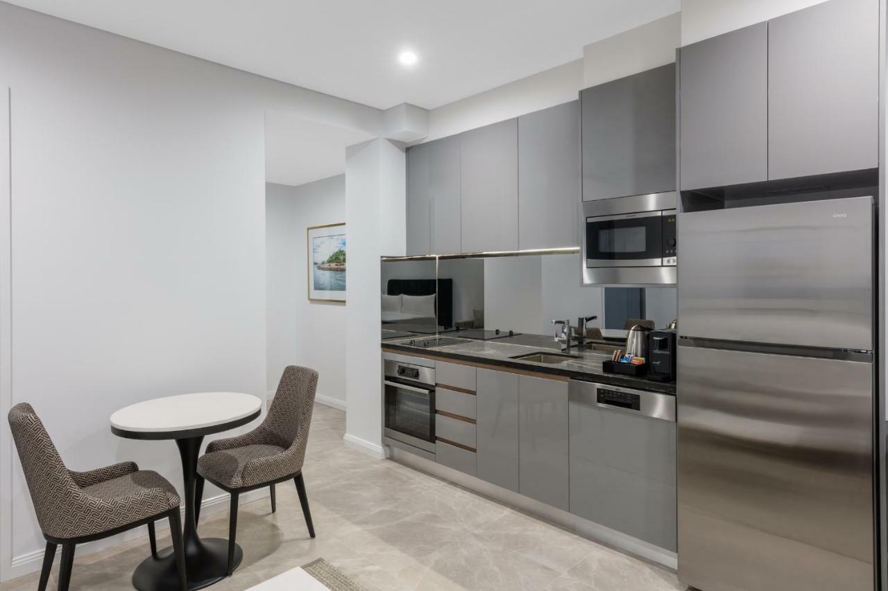 Meriton Suites Sussex Street, Sídney Exterior foto The photo shows a modern kitchen area that features a sleek design. The cabinetry and appliances are in shades of gray, giving it a contemporary look. There is a stainless steel refrigerator, microwave, and oven, along with a sink and cooking area. 
